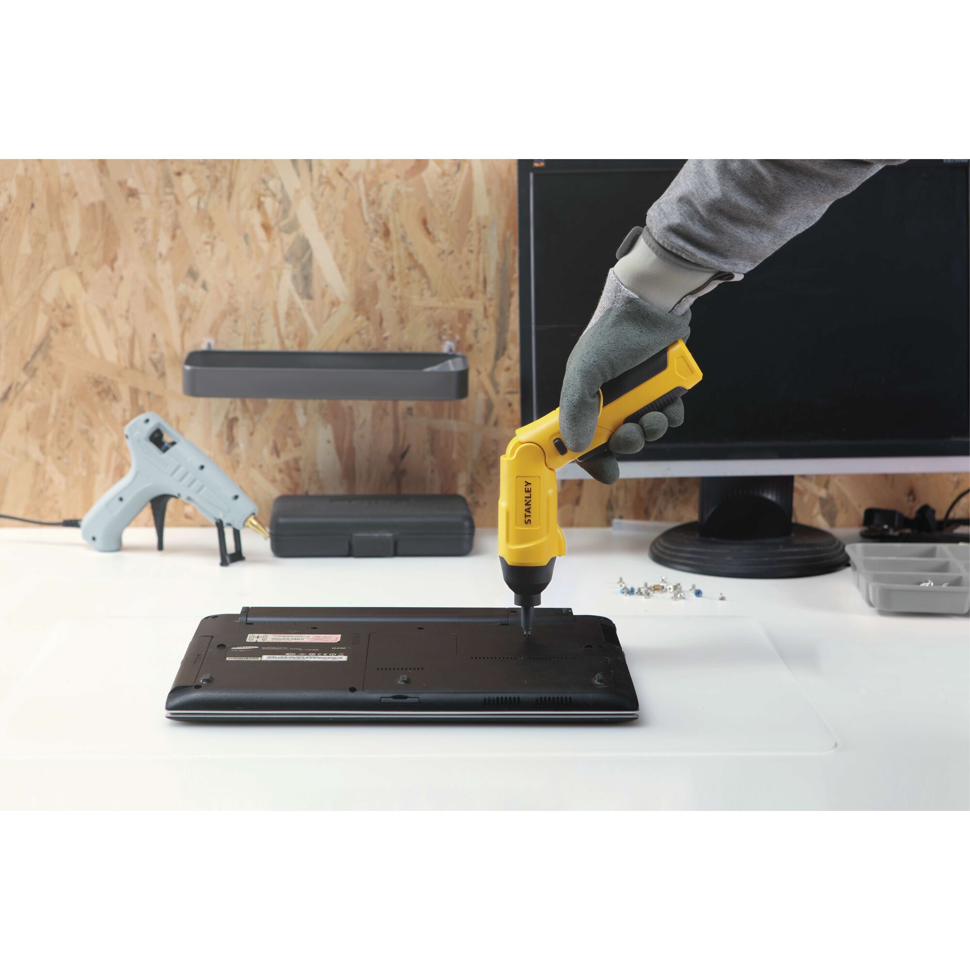 Photo of STANLEY SCS4K cordless screwdriver being used to repair a laptop on a desk, workshop setting.