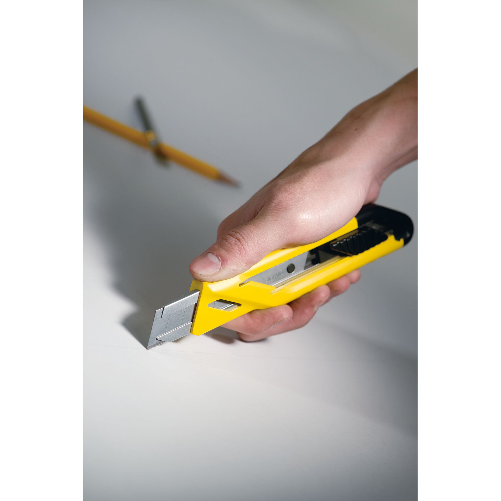 STANLEY STHT10265-8 utility knife with yellow handle held in hand, cutting white surface.