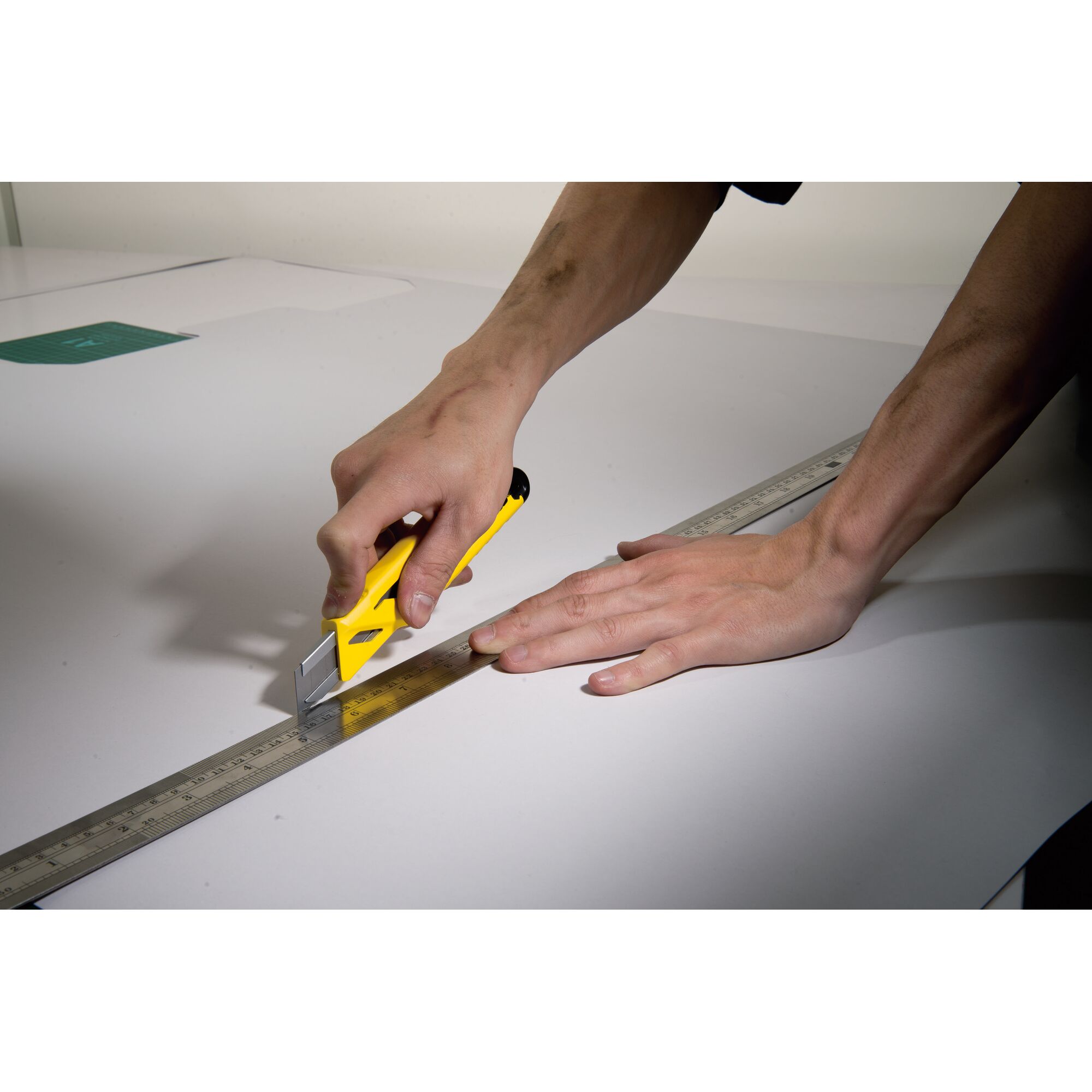 STANLEY STHT10265-8 utility knife in yellow being used to cut along a metal ruler on a white surface, top view.