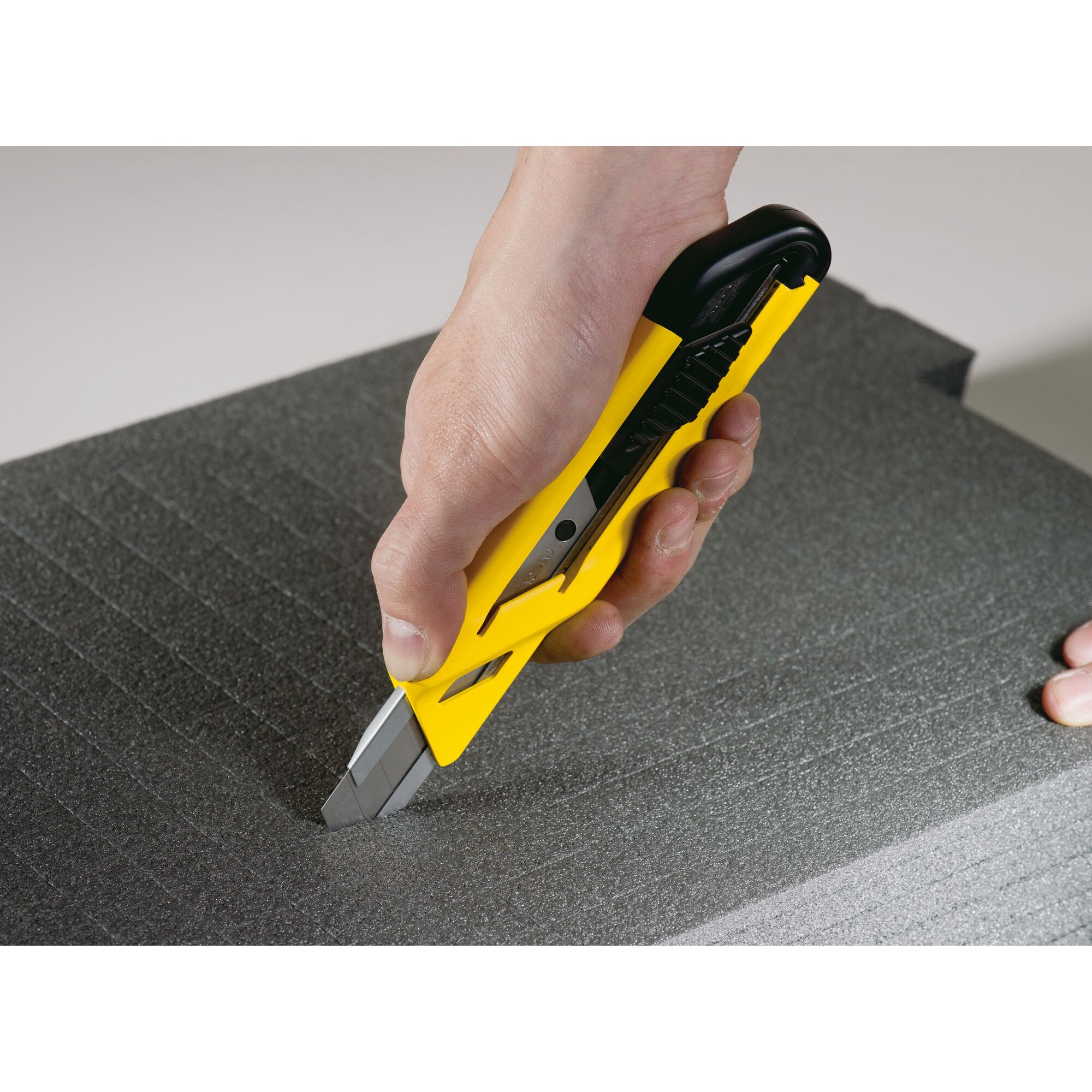 STANLEY STHT10265-8 utility knife cutting foam board, close-up of yellow and black handle.