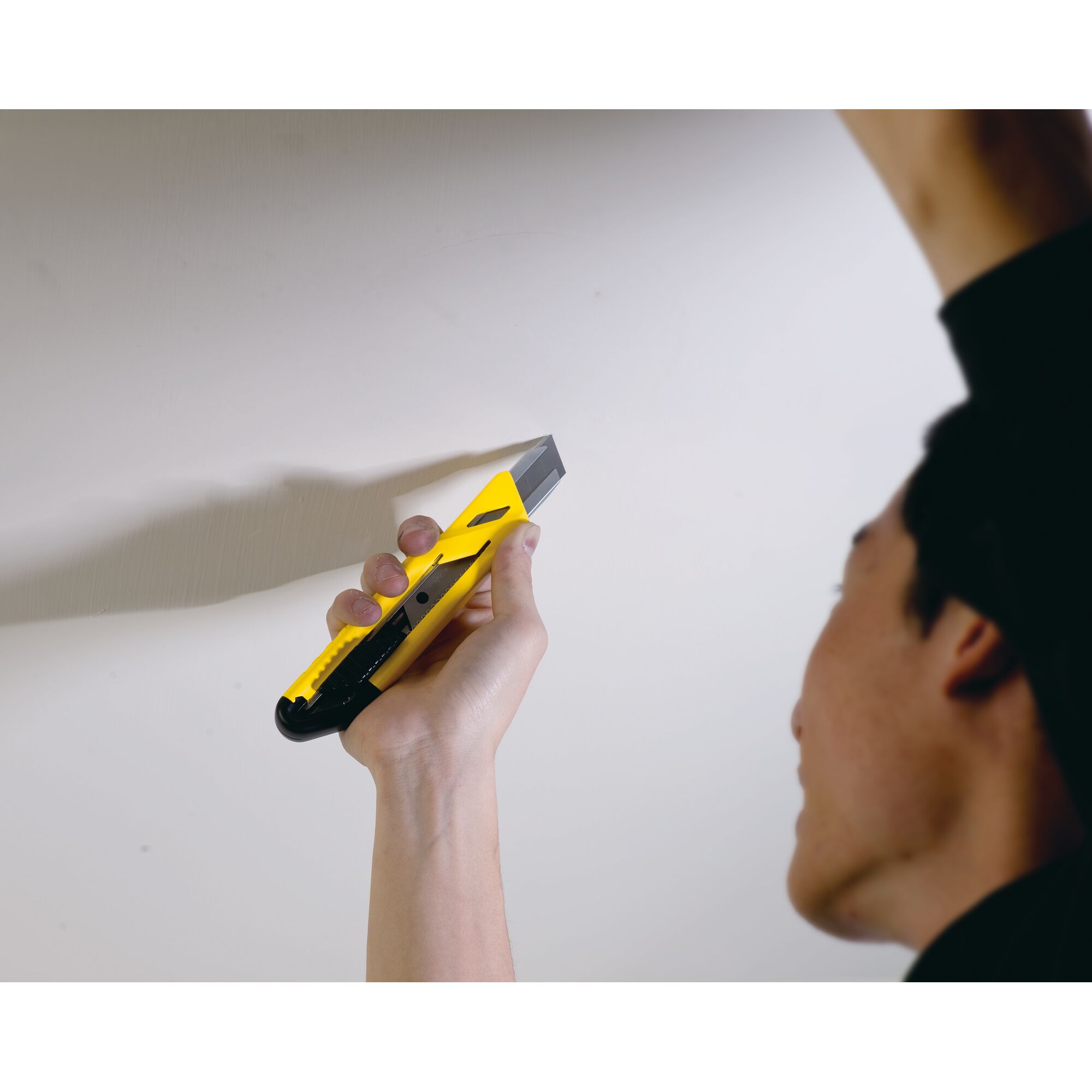 Photo of STANLEY STHT10265-8 utility knife in hand cutting along wall, yellow and black handle visible.