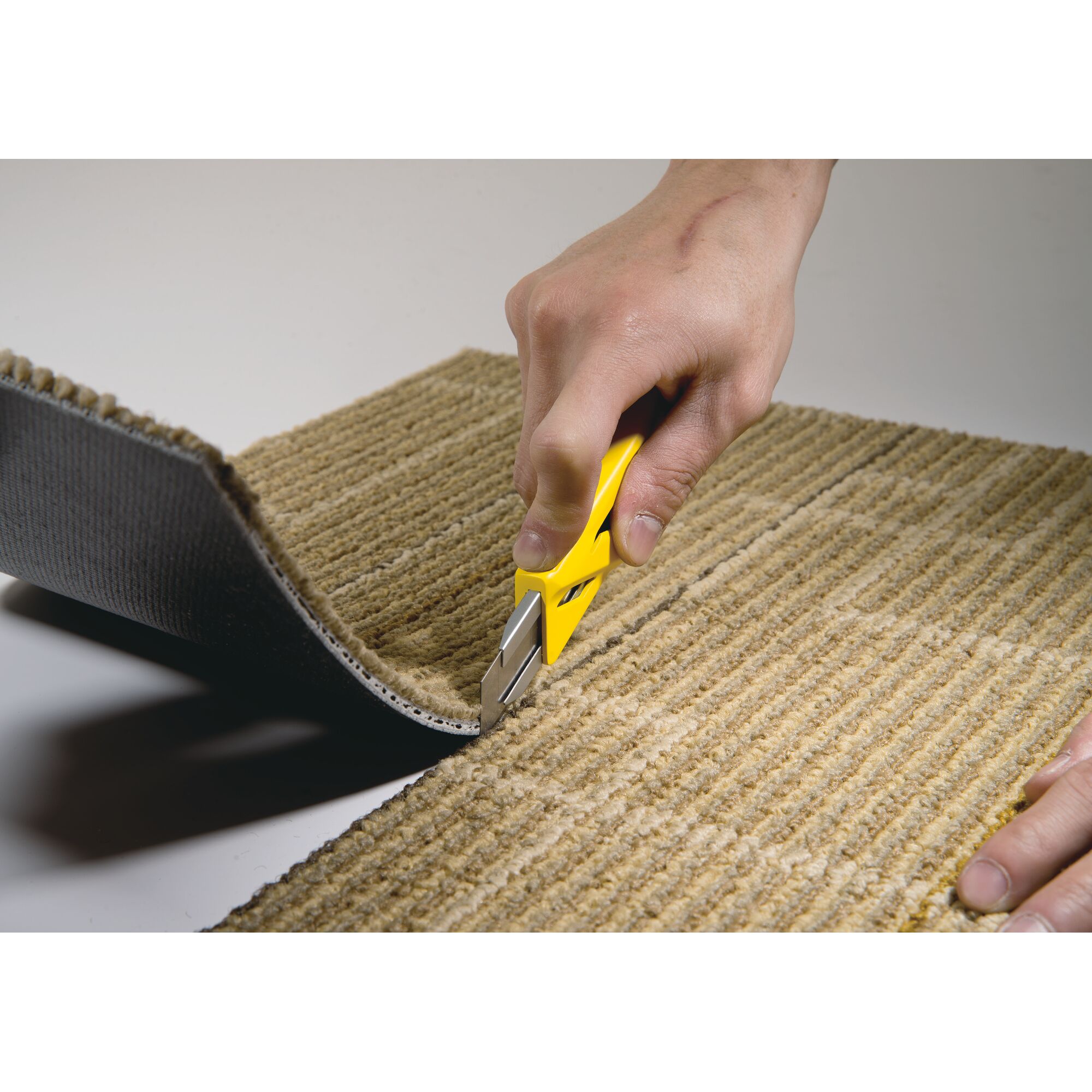 STANLEY STHT10265-8 utility knife cutting beige carpet, close-up photography.
