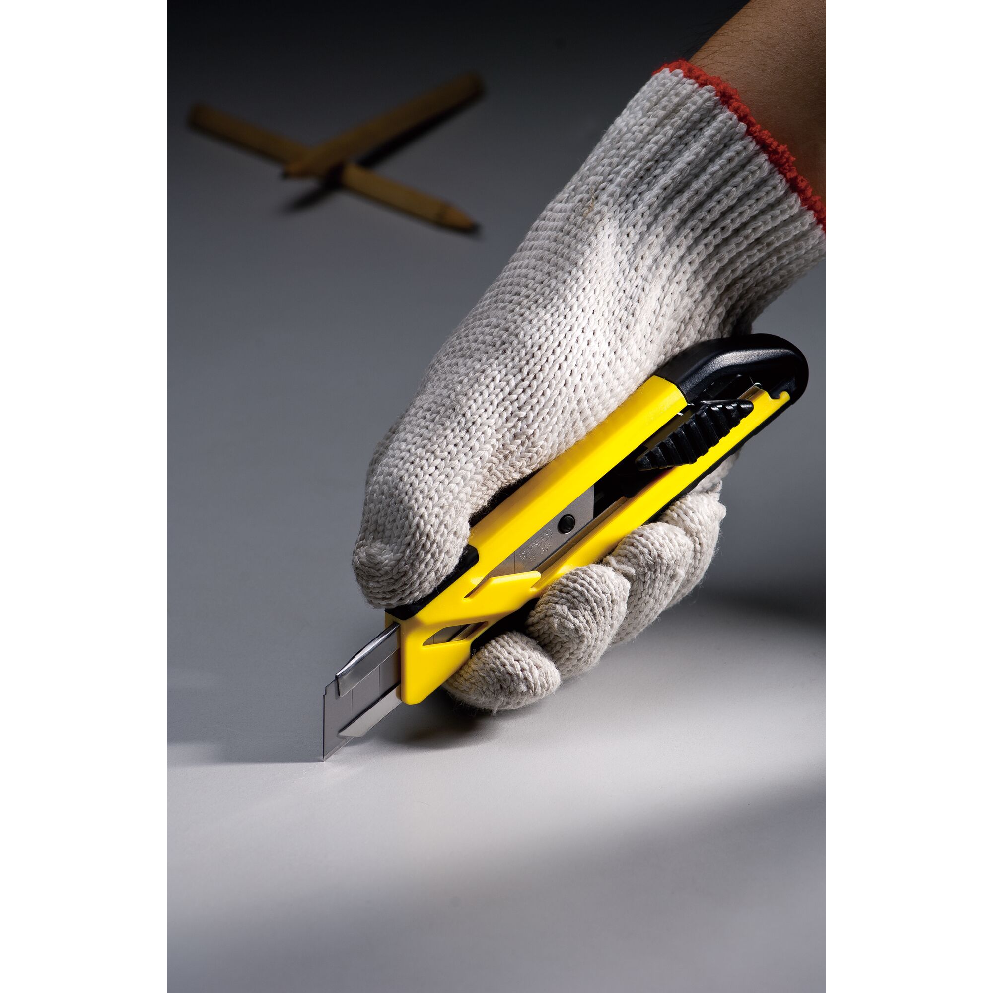 Photo of STANLEY STHT10266-8 utility knife in a gloved hand, yellow and black design, blade extended.