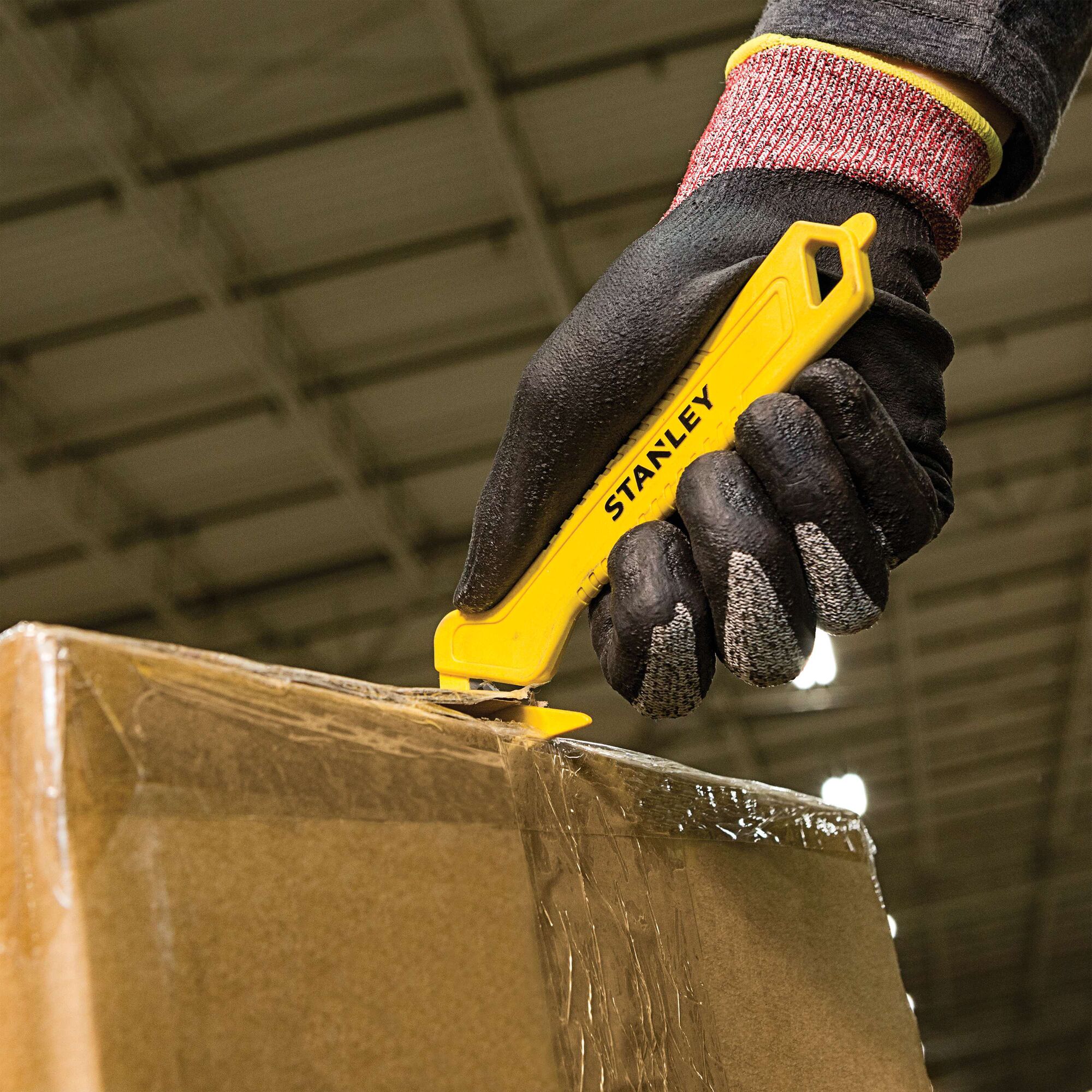 Photo of STANLEY STHT10355 utility knife cutting cardboard box, worker wearing black glove.