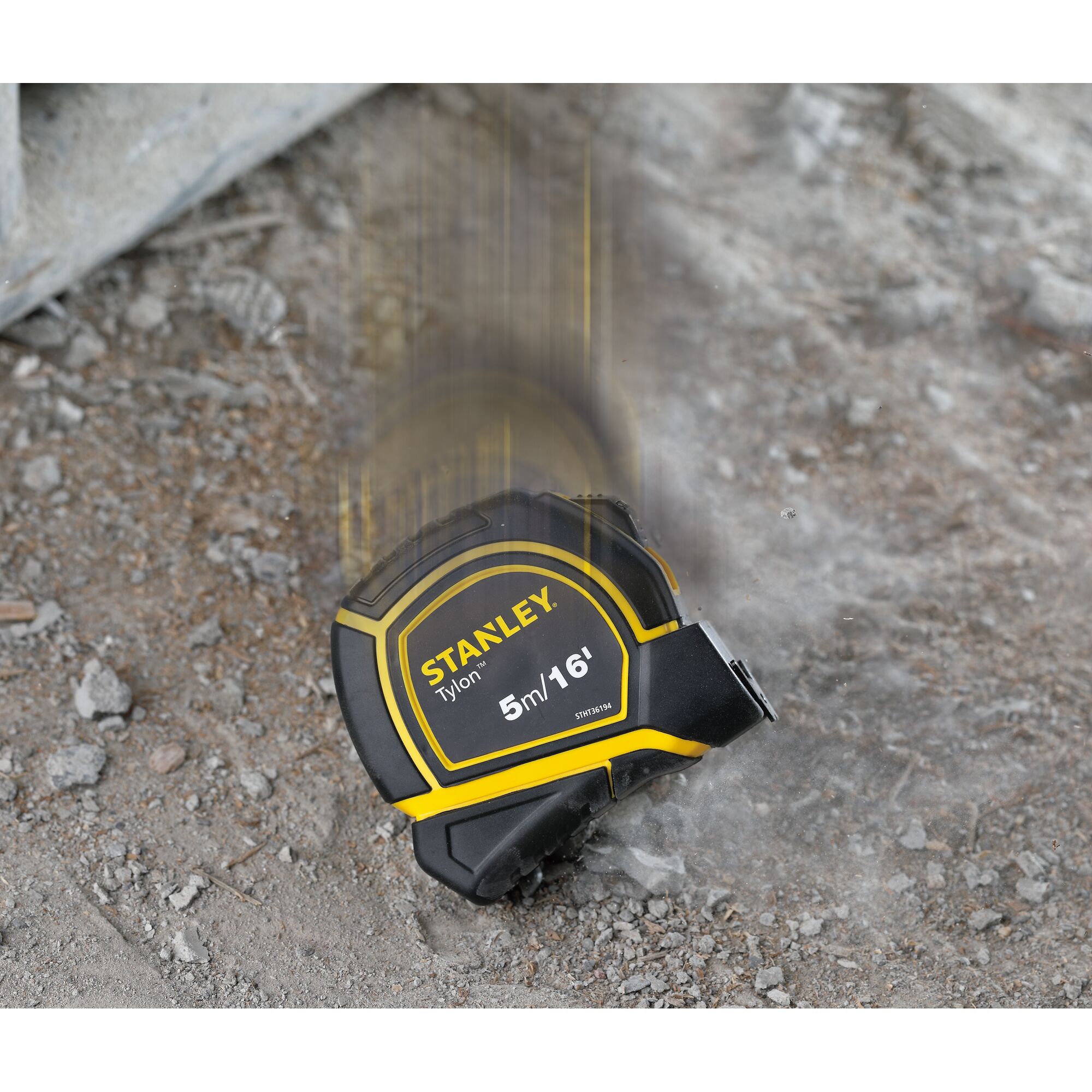 Stanley STHT36194 tape measure in black and yellow dropped on rough ground, side view.