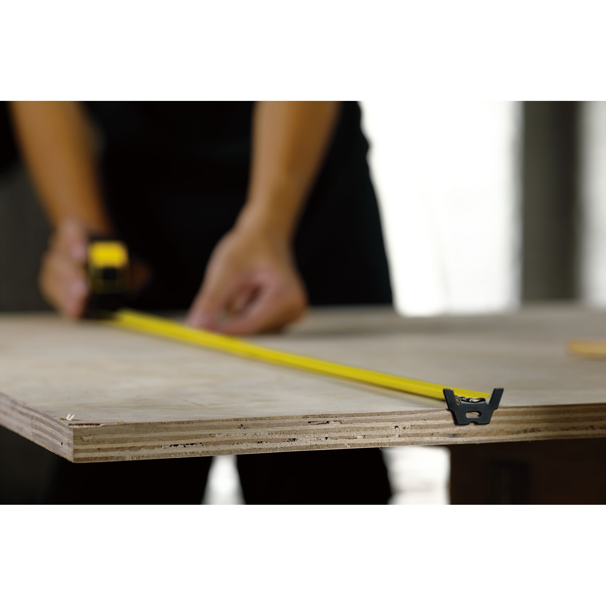 STANLEY STHT36195 yellow tape measure extended across plywood, close-up side view, photography.