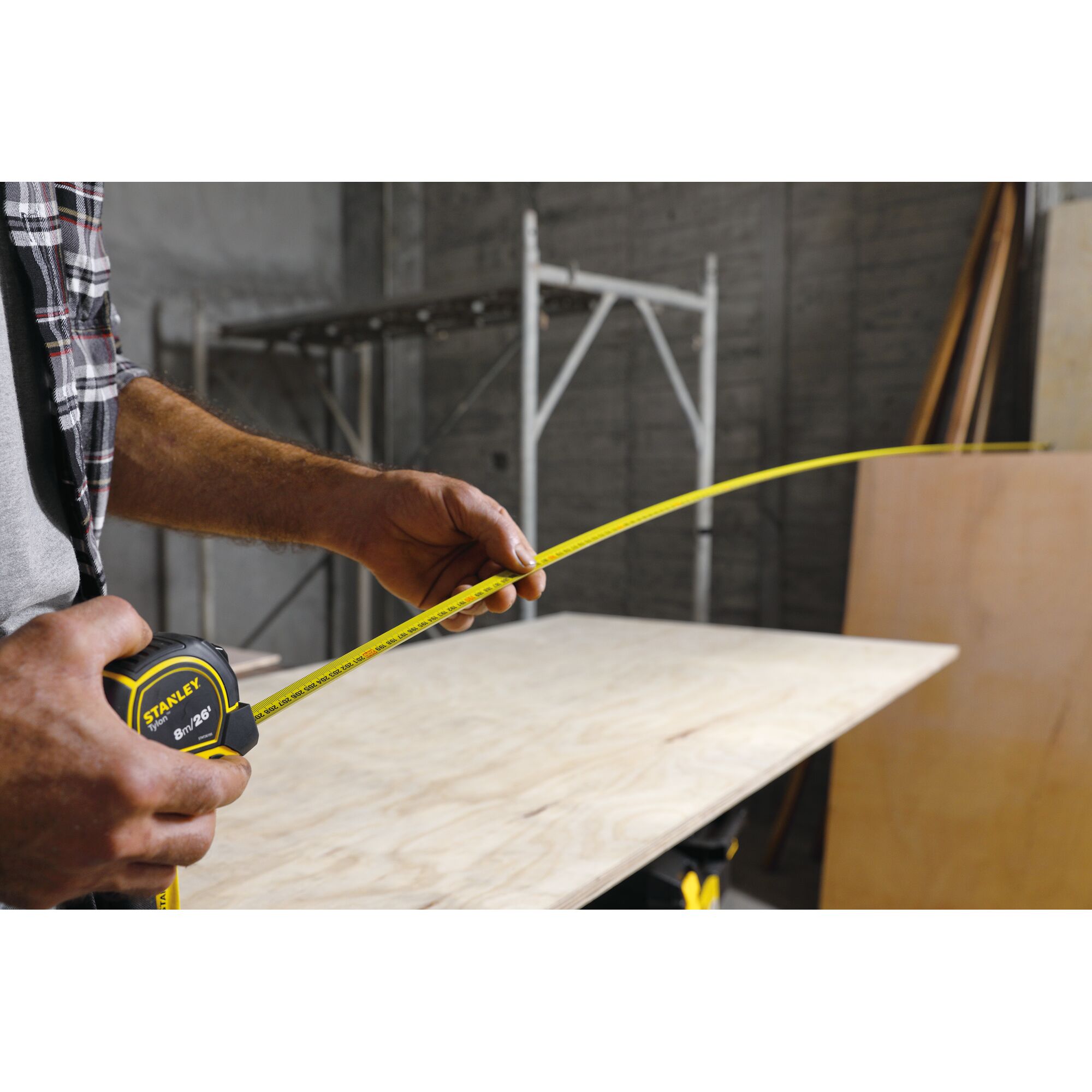 STANLEY STHT36195 tape measure in use measuring plywood sheet on workshop table.