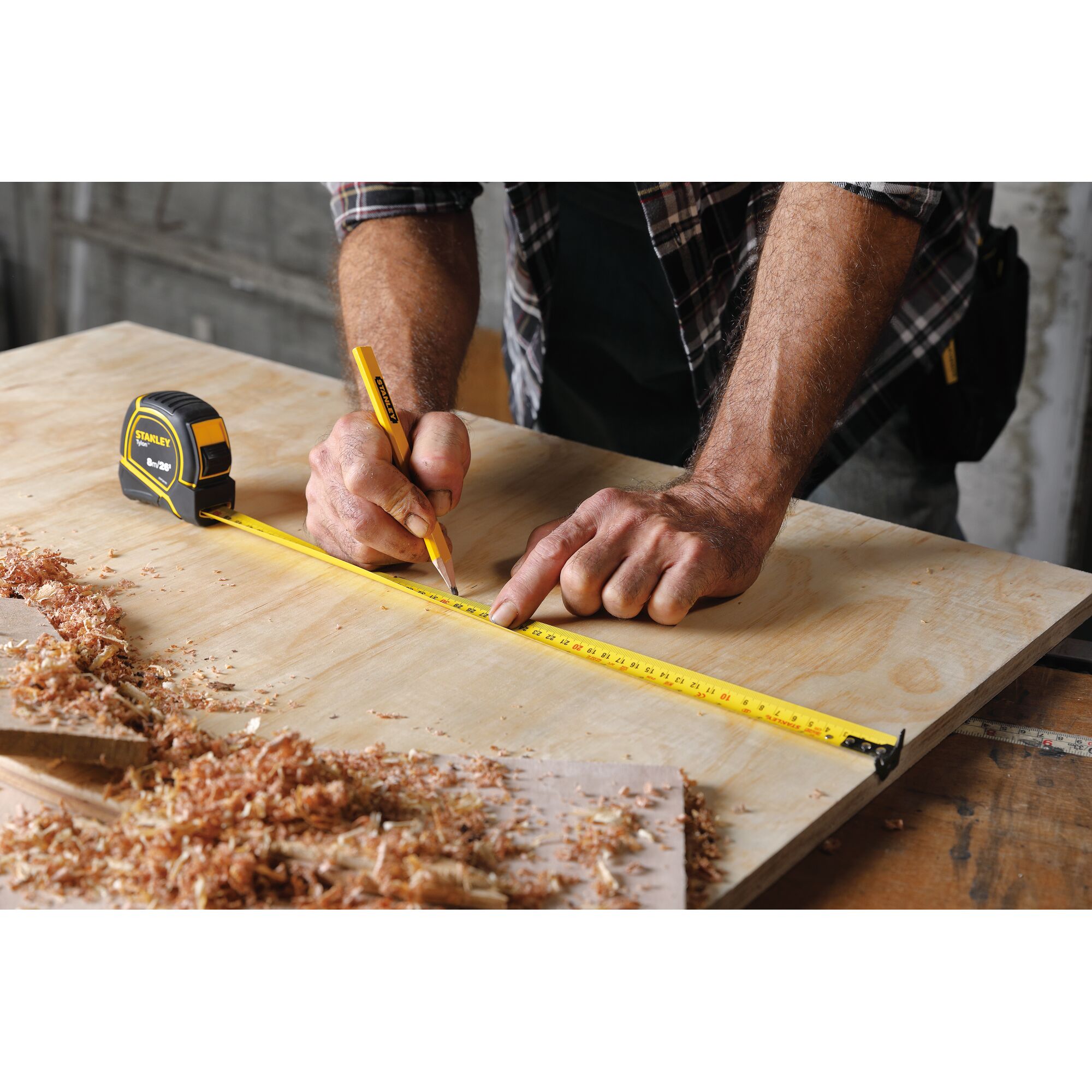 Stanley STHT36195 tape measure in use on plywood, yellow blade extended for marking measurements.
