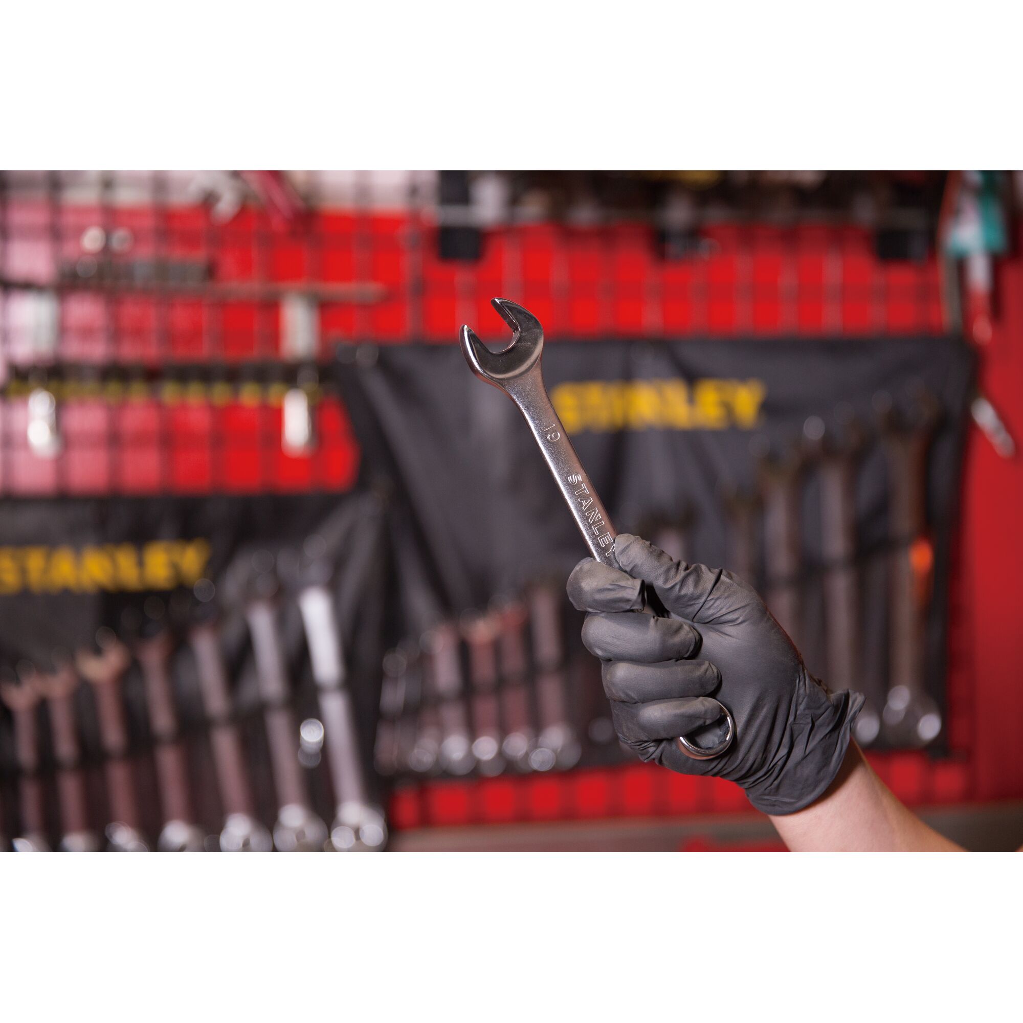 Photo of STANLEY STMT80233-8 open-end wrench held in gloved hand, tool rack visible in background.