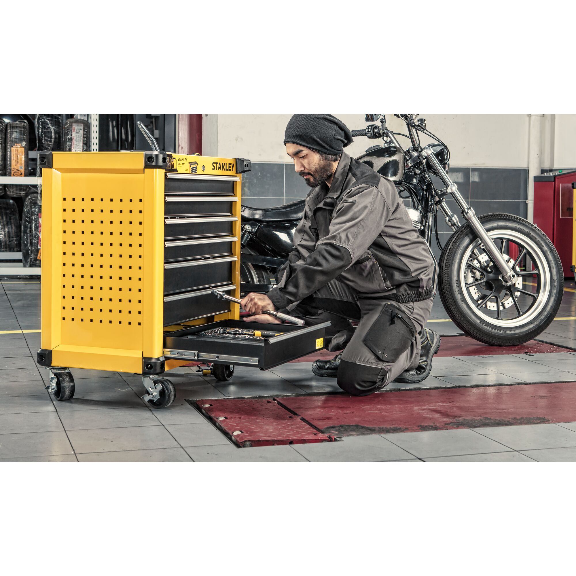 Stanley STST74306-8 yellow tool chest with drawers in workshop, mechanic using bottom drawer near motorcycle.